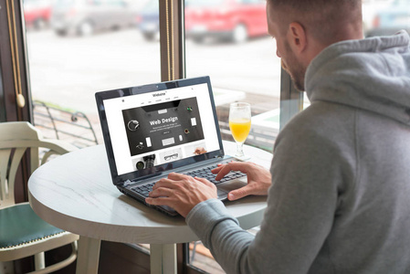 访客在他的笔记本电脑上打开一个负责设计公司的网站。咖啡店背景