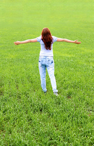 站在绿色田野的快乐女人。举起手来。一个十几岁的女孩的后方视图