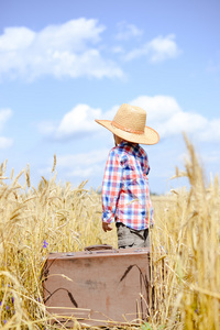 小男孩戴着草帽，带着手提箱在麦田里