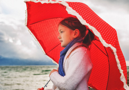 小女孩用大红色的伞，旁边湖在很冷的一天