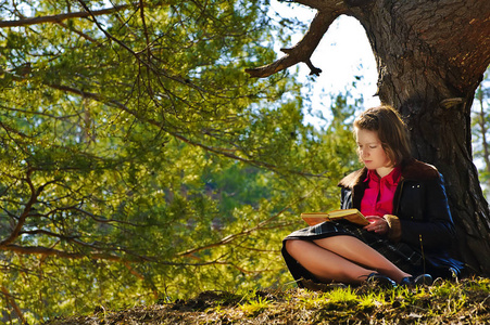 一个女孩正在读一本书在一个秋天的树林