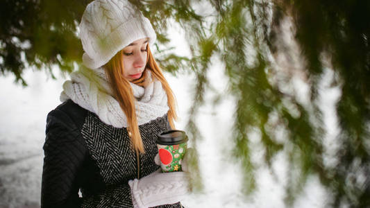 白色的围巾，帽子的可爱女人肖像针织外套上的雪的户外背景和模糊冷杉的枝条在冬天