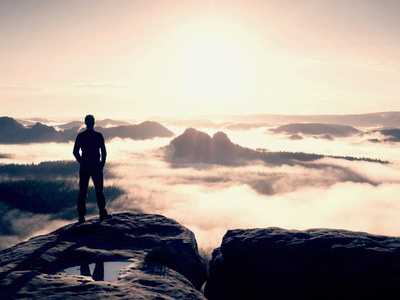 徒步旅行者的身影站在悬崖，看着在迷雾笼罩的山谷到太阳蓝色 filtere
