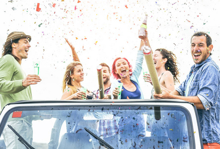 一群快乐的朋友在可兑换的吉普车上投掷五彩纸屑年轻人庆祝和有乐趣喝香槟和笑一起户外青年生活方式概念