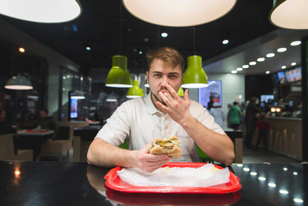 一个英俊的男人吃汉堡包在快餐和的手指