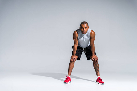 全长度观看运动的年轻的非洲裔美国运动员站在膝盖上, 看着在灰色的摄像头