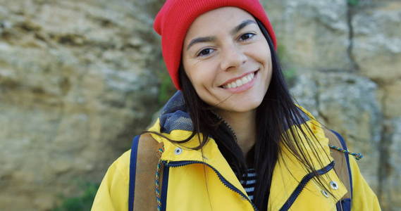 美丽的年轻女子在红色的帽子向上看, 然后进入在岩石背景的摄像头。寒冷晴朗的一天。肖像拍摄。外