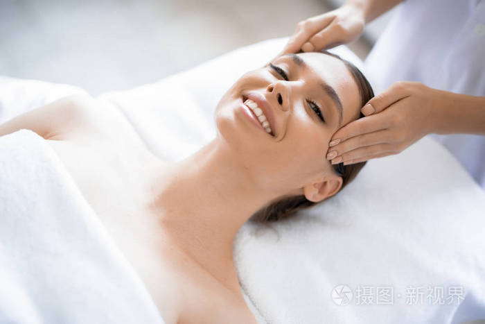 在美容院享受面部水疗按摩的年轻微笑的妇女