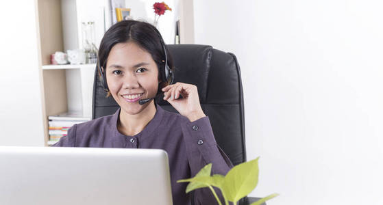 亚洲妇女快乐微笑客户支持操作员与耳机在办公桌上的办公室。带有复制空间的全景横幅