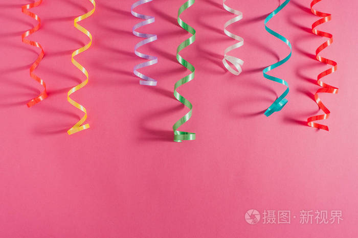 五颜六色的党丝带彩带在粉红色明亮的背景.聚会或生日概念
