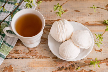美丽的成分, 杯茶和棉花糖。春季早餐。一杯茶, 白色棉花糖在木质背景。绿芽叶的树枝
