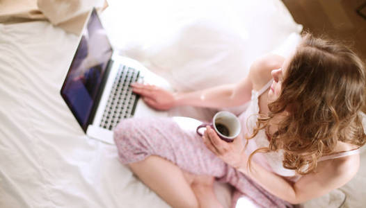 年轻漂亮的女人，坐在床上用笔记本电脑