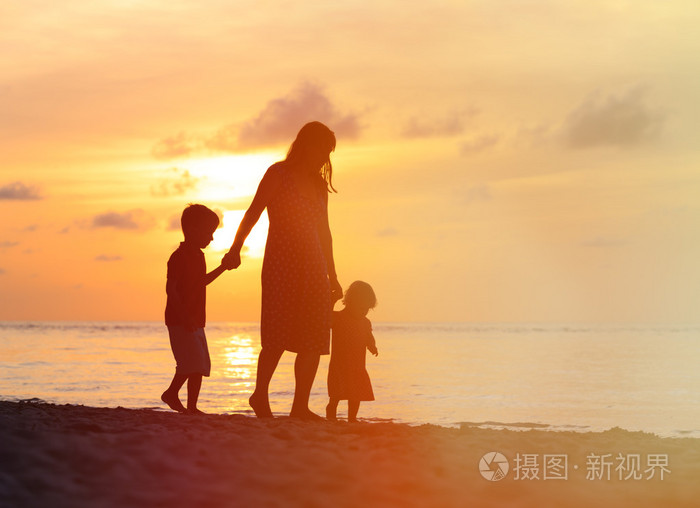 母亲和两个孩子在日落时在海滩上行走