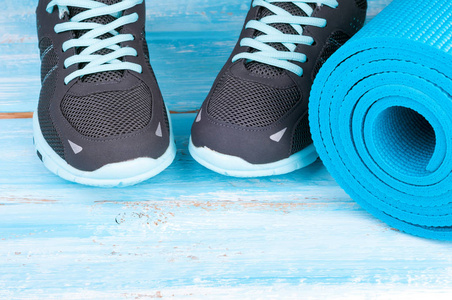 运动器材和运动鞋。瑜伽垫和体育鞋在蓝色木背景。概念的健康生活方式 健康食品 运动和饮食