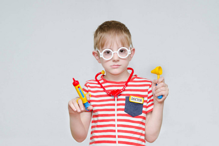 沉思的男孩在玩医生。玩具注射器, 眼镜和 phonendoscope
