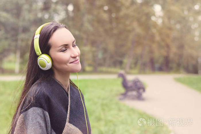 年轻快乐的女人听音乐从智能手机与耳机在一个安静的公园