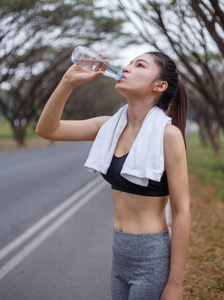 在公园里年轻的运动型女人喝水