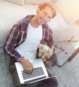 与笔记本电脑抱着他的狗和坐在旁边沙发上的帅哥