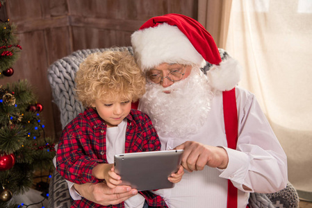 圣诞老人与孩子在使用平板电脑的膝盖上