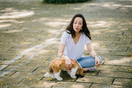 一个年轻的泛亚洲妇女的肖像坐在她年轻的石 tzuh 小狗在公园里的一天。她在微笑, 他们都在享受温暖的一天。