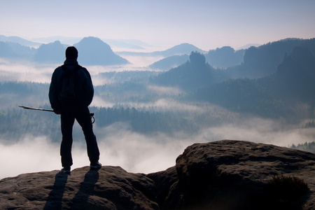 在洛矶山脉有雾的日子。旅游与剪影手杆。徒步旅行者站在岩石看法点上方迷雾笼罩的山谷