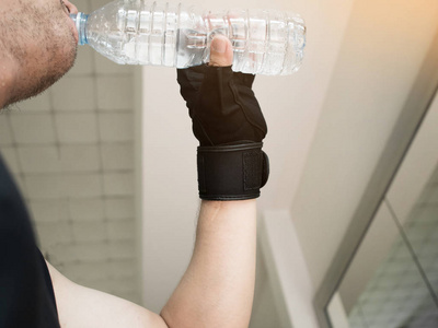 人的双手戴上手套拿着瓶水在健身房