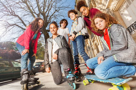 在城市街道上, 有滑板或旱冰鞋的青少年男孩和女孩的低角度视图