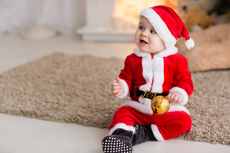 有趣的婴儿男孩穿着圣诞老人的帽子与金色圣诞球