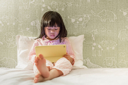 穿着睡衣的小女孩在床上玩平板电脑