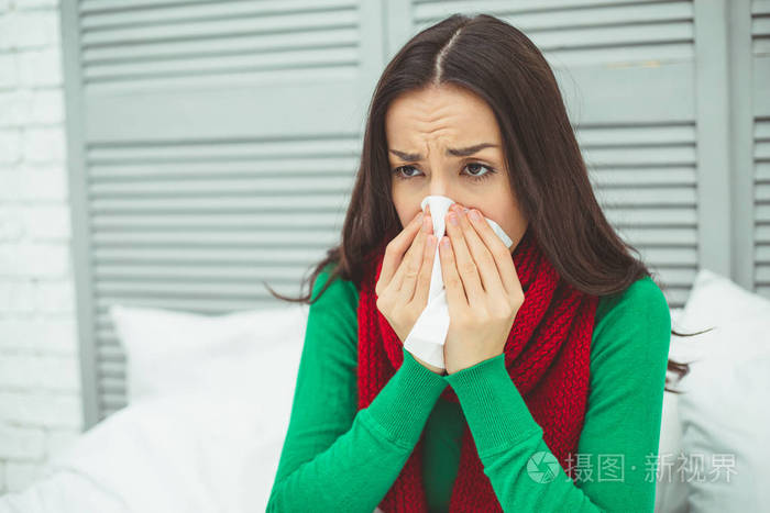 关闭一个年轻的生病的女人的肖像, 流鼻涕的红围巾躺在家里的床上和