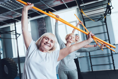 快乐的妇女与棍子做侧弯锻炼在健身房