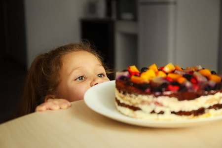 可爱的小女孩去品尝在厨房桌上留下的甜蛋糕