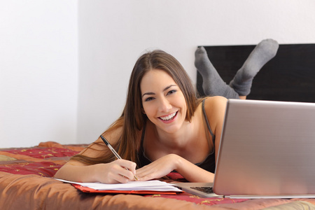 快乐的学生学习与她的卧室里的一台笔记本电脑