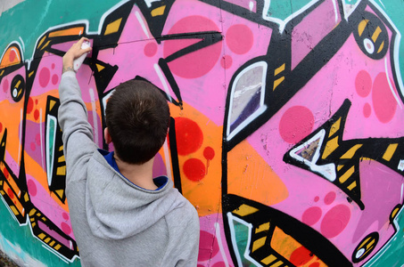 一个穿着灰色帽衫的年轻人在雨天的墙上画着粉红色和绿色的涂鸦。鱼眼射击