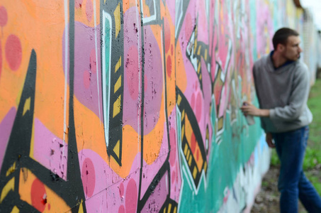 穿着灰色上衣的年轻人在雨天的墙上画着粉红色和绿色的涂鸦聚焦在墙上的碎片和模糊的艺术家