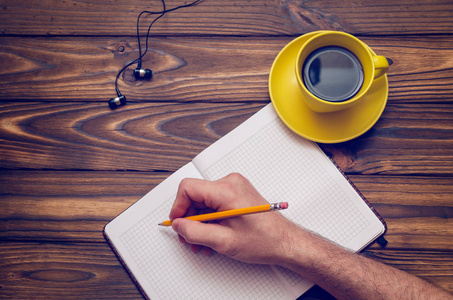 一个男人用一张木桌上的黄色咖啡杯在笔记本上写东西