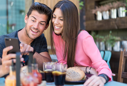 快乐的年轻夫妇座位在餐厅露台与智能手机