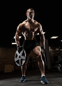 英俊的男人用大块的肌肉，在健身房中的相机摆姿势