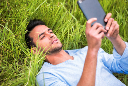 年轻漂亮的严重商业男人躺在绿色的草地，在设备上看