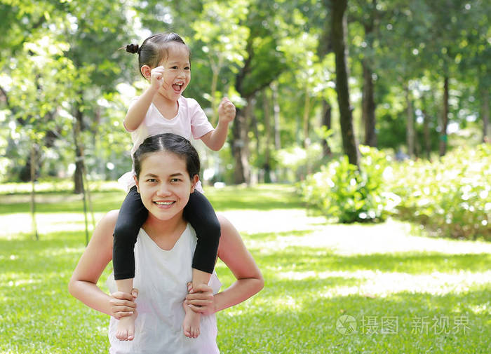 儿童女孩玩骑在母亲的脖子在公园