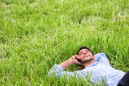 快乐的梦想的年轻商业人躺在绿色的草地上。在电话上交谈