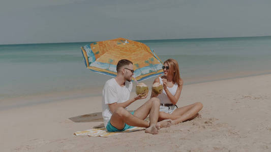 在阳光明媚的暑假里, 在热带海滩上喝椰奶的年轻快乐情侣