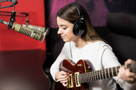 年轻女歌手在广播电台演奏吉他和唱歌在话筒