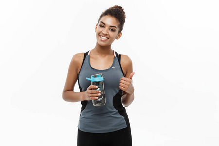 健康和健康的概念美丽的非洲裔美国女孩运动服装举行饮水瓶后锻炼。在白色工作室背景下被隔离