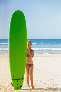 穿着比基尼的年轻可爱的女孩摆在绿色冲浪板附近