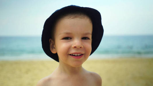 在海边的海滩上看着摄像机的男孩肖像
