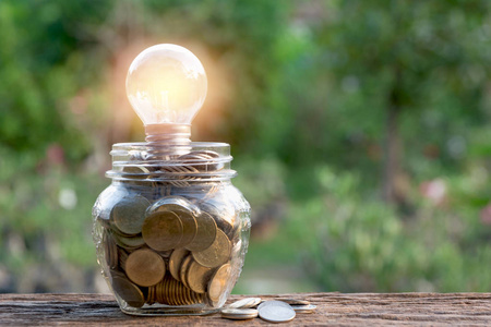 节能灯泡和硬币在玻璃罐上的自然背景。储蓄会计和财务概念