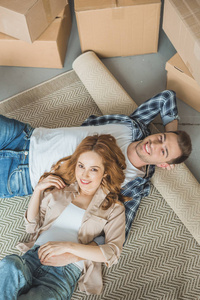 在搬迁期间躺在轧毯上的快乐年轻夫妇微笑着拍照