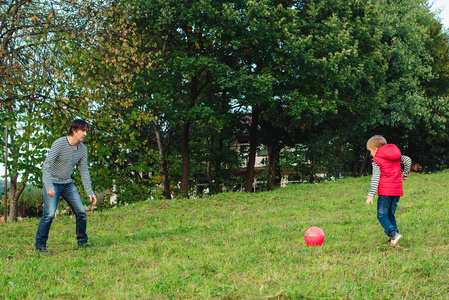 年轻的父亲与他的小儿子在绿色草地上踢足球