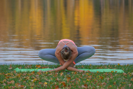 年轻女子在河附近的秋市公园做瑜伽
